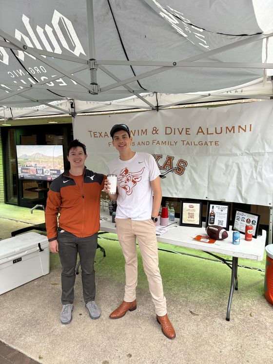 Two guests at the Texas Swim & Dive Alumni Friends and Family Tailgate banner.